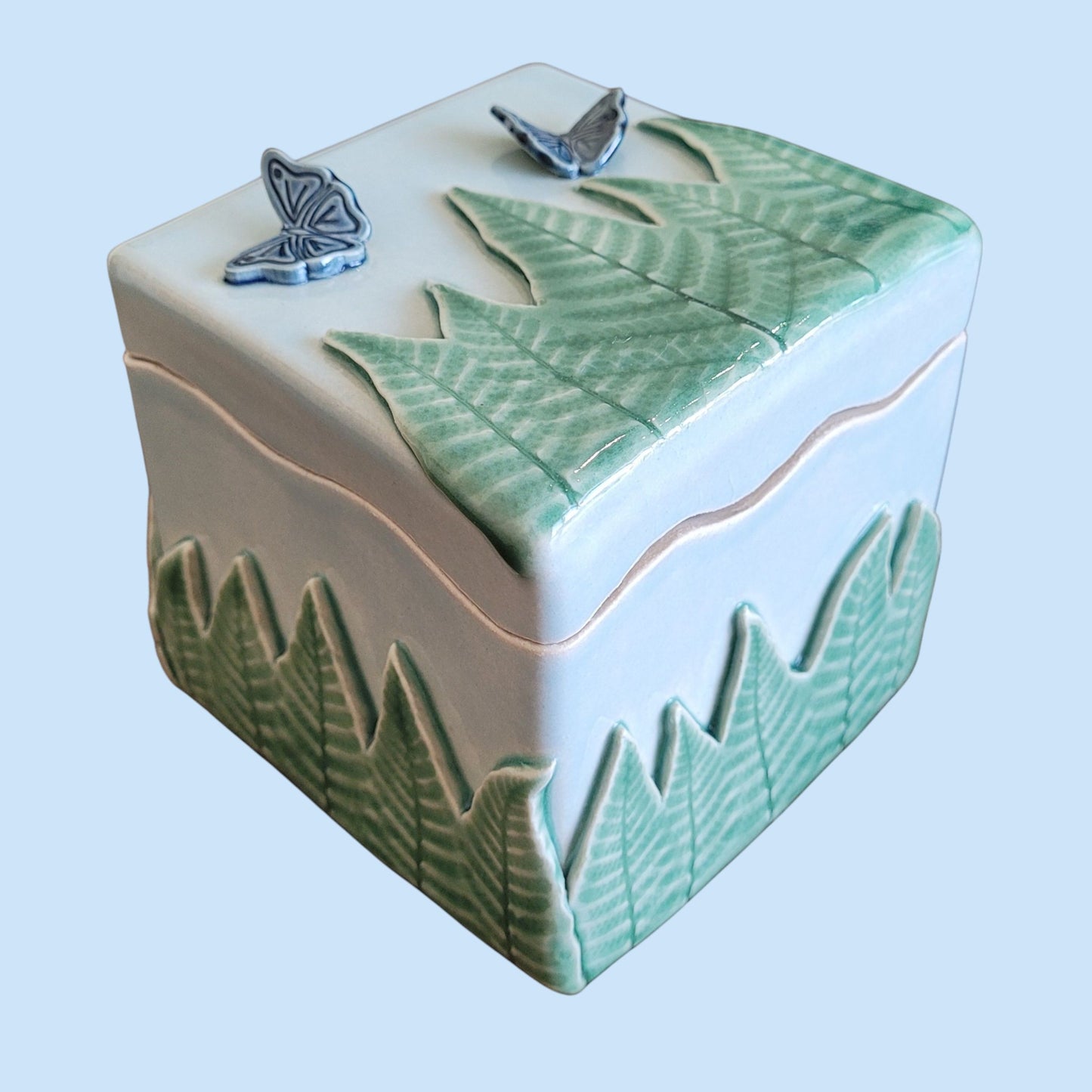 Decorative ceramic box with leaf patterns and blue butterflies on a light blue background