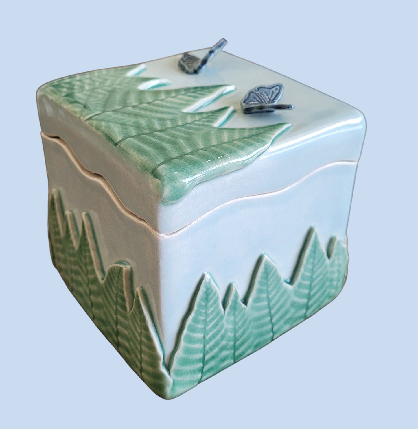 Ceramic box with green ferns and blue butterflies on a light blue background