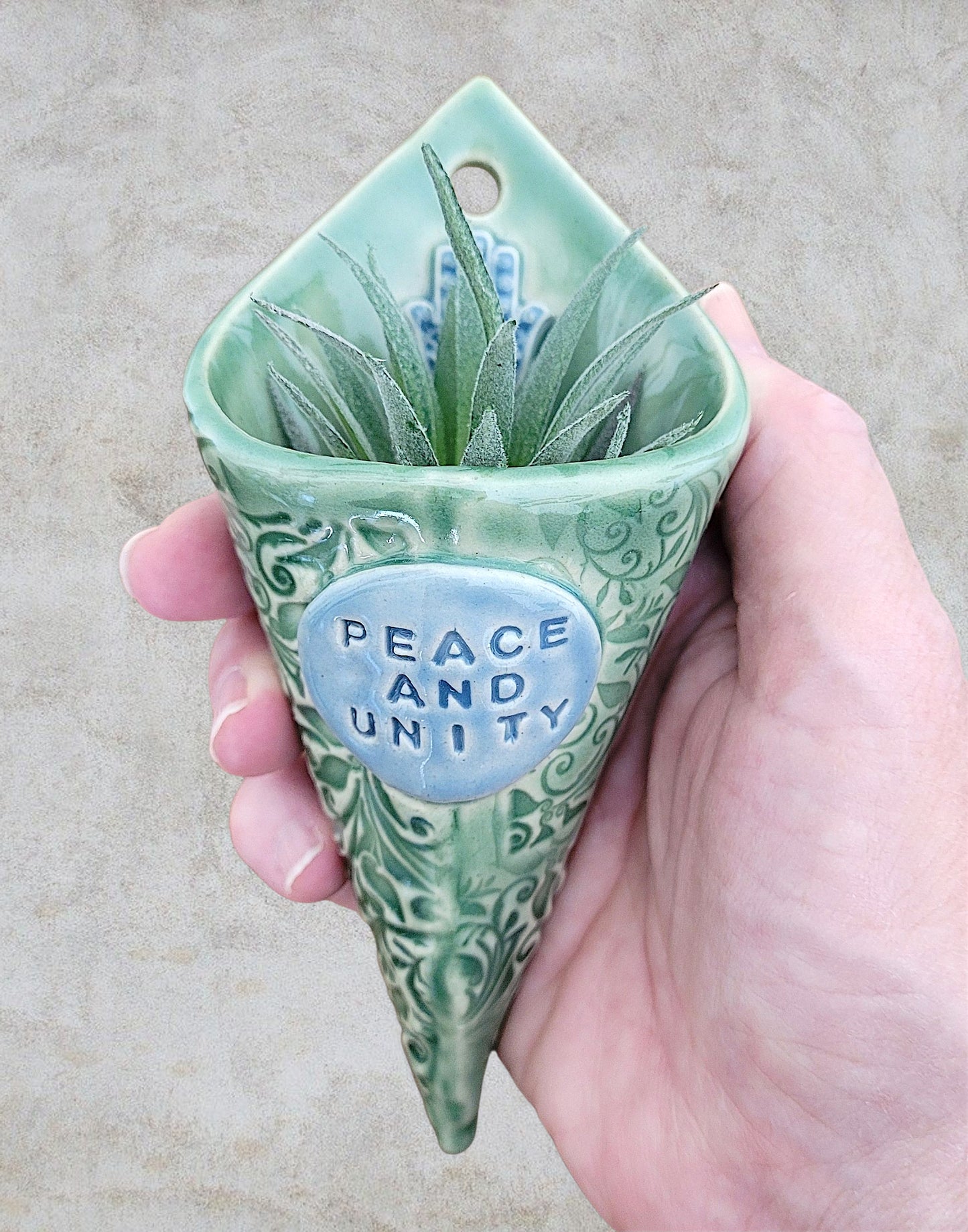 Green ceramic planter with 'Peace and Unity' text held in a hand against a neutral background