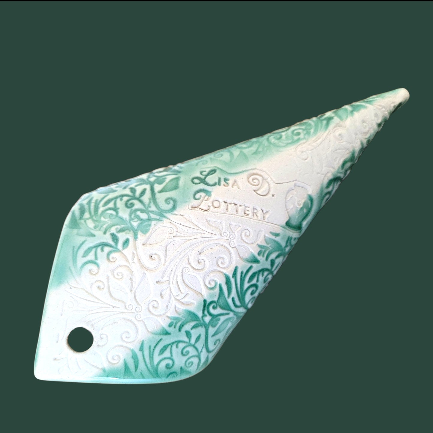 Reverse side of decorative ceramic wall hanging with intricate patterns showing the Lisa D Pottery "Maker's Mark" on a green background
