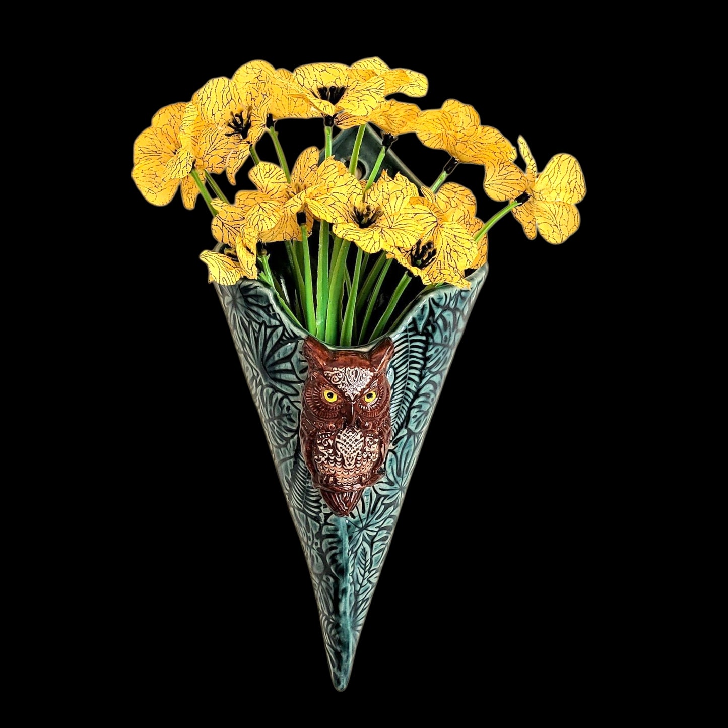 Decorative vase with owl design holding yellow flowers on a black background