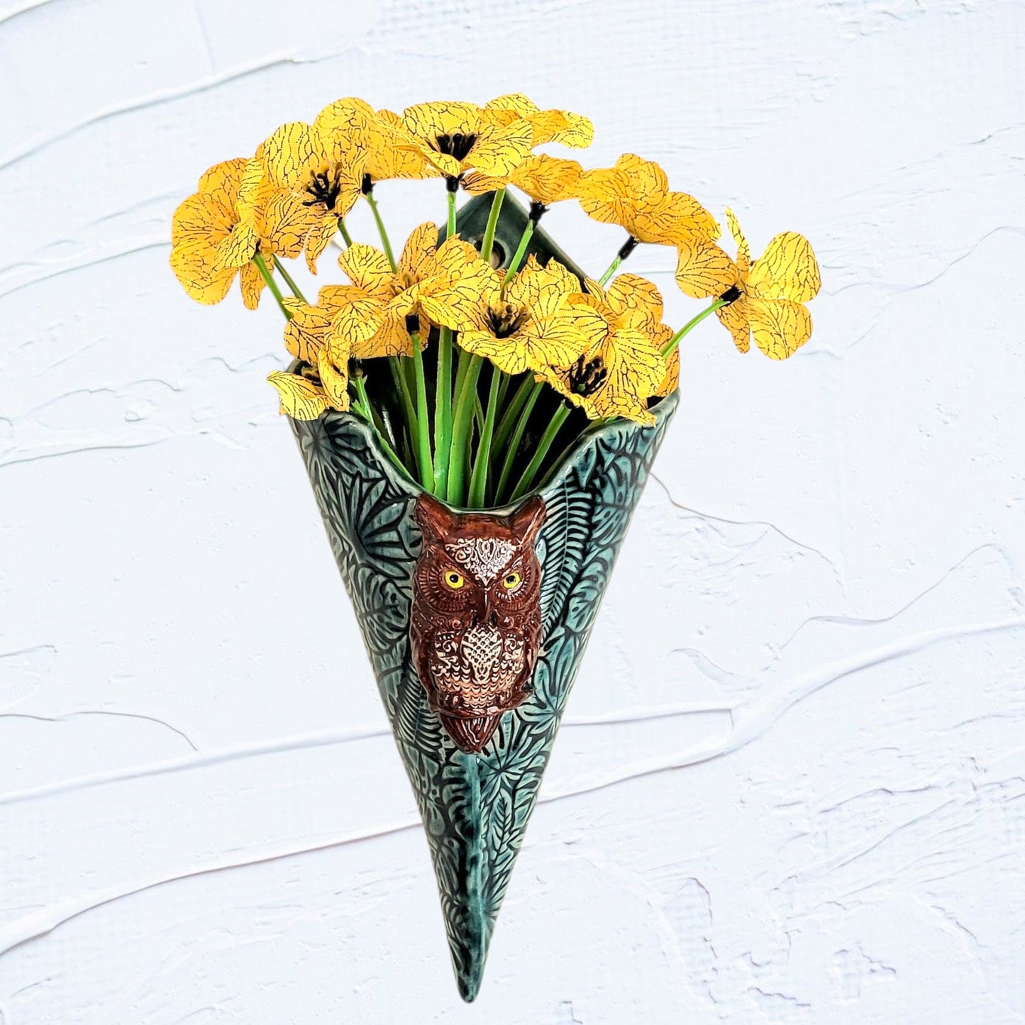 Decorative vase shaped like a cone with an owl design, filled with yellow flowers on a light gray background.