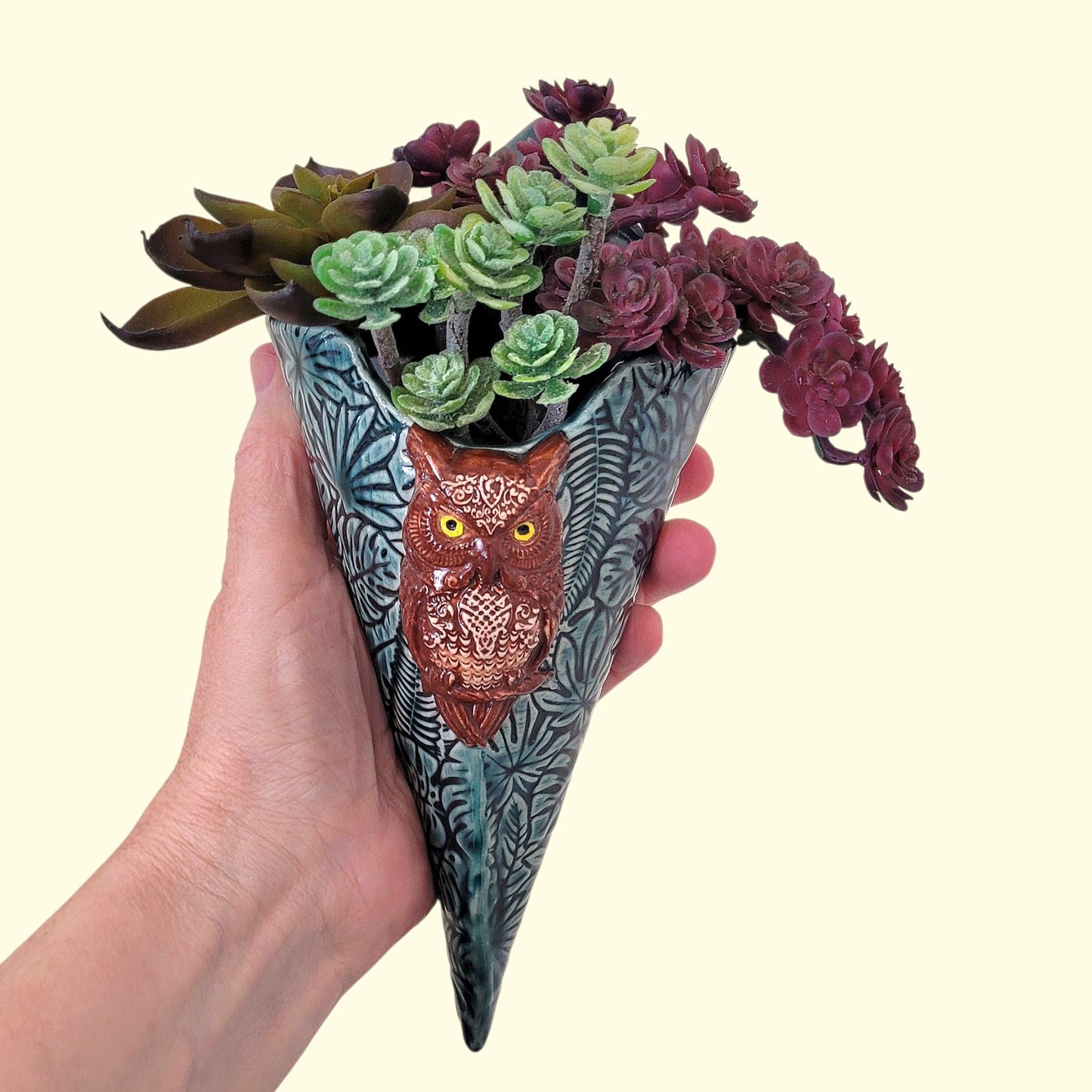 Hand holding a cone-shaped planter with owl design and succulents on a light background