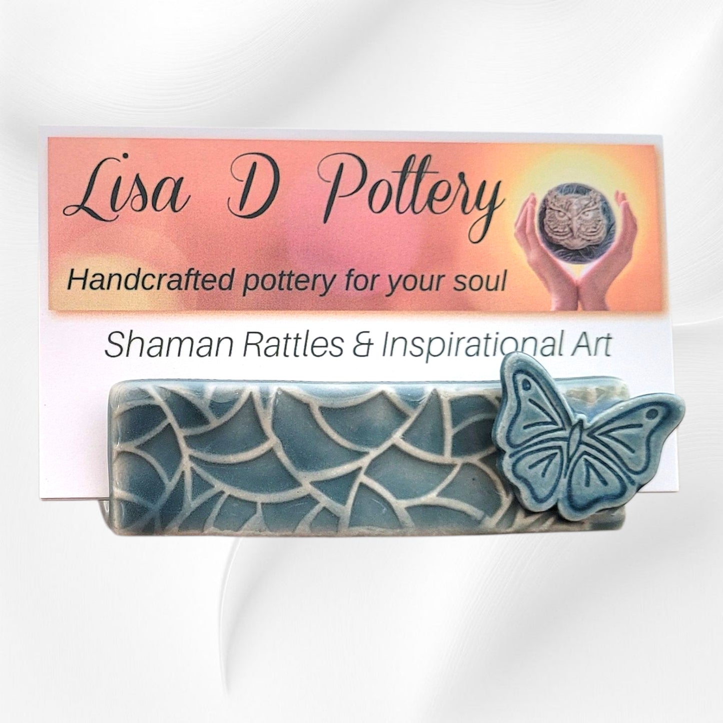 Ceramic business card holder with butterfly design and 'Lisa D Pottery' branding on a gradient background