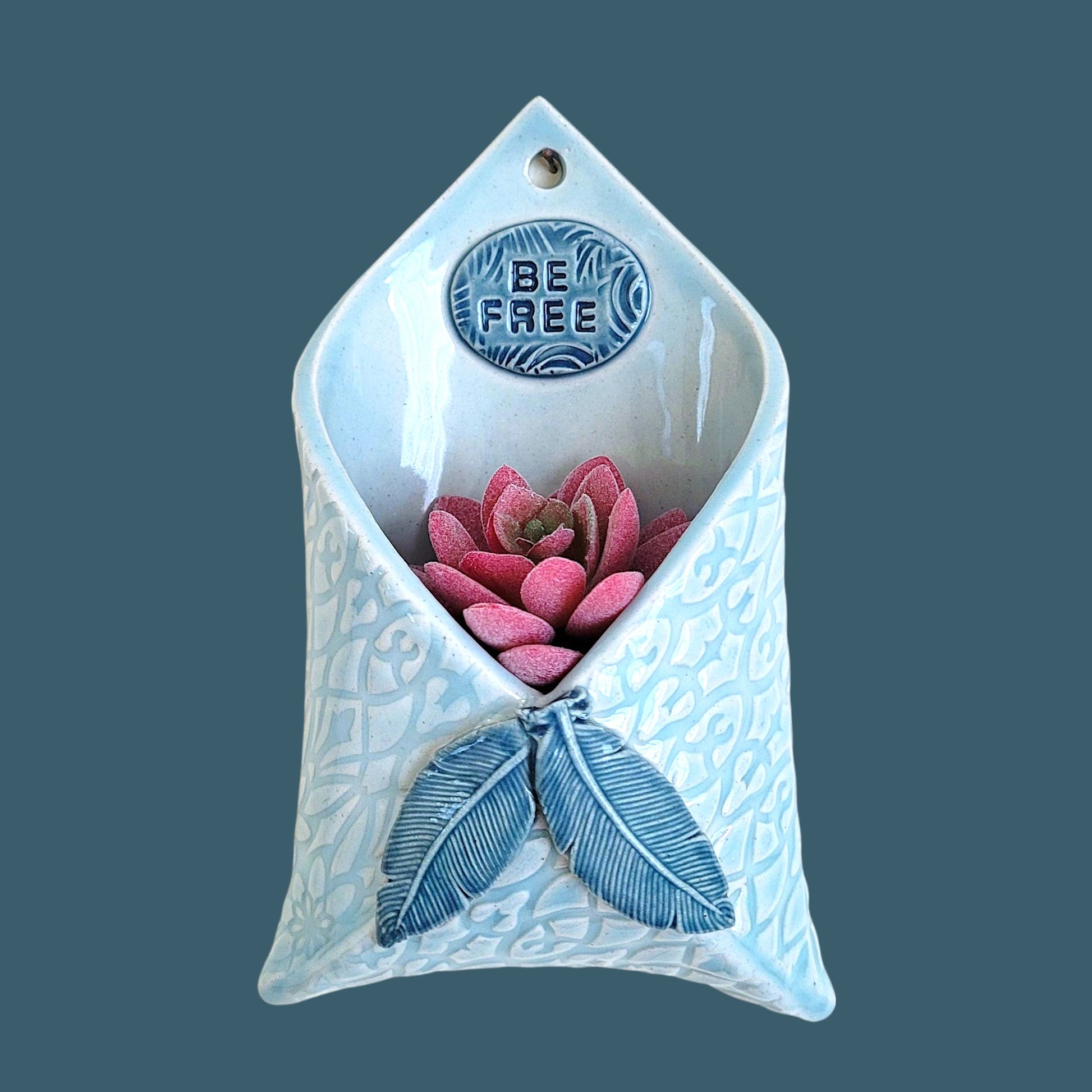 Handcrafted stoneware wall pocket featuring natural feather design with 'Be Free' inspirational message, glazed ceramic art piece for home decor