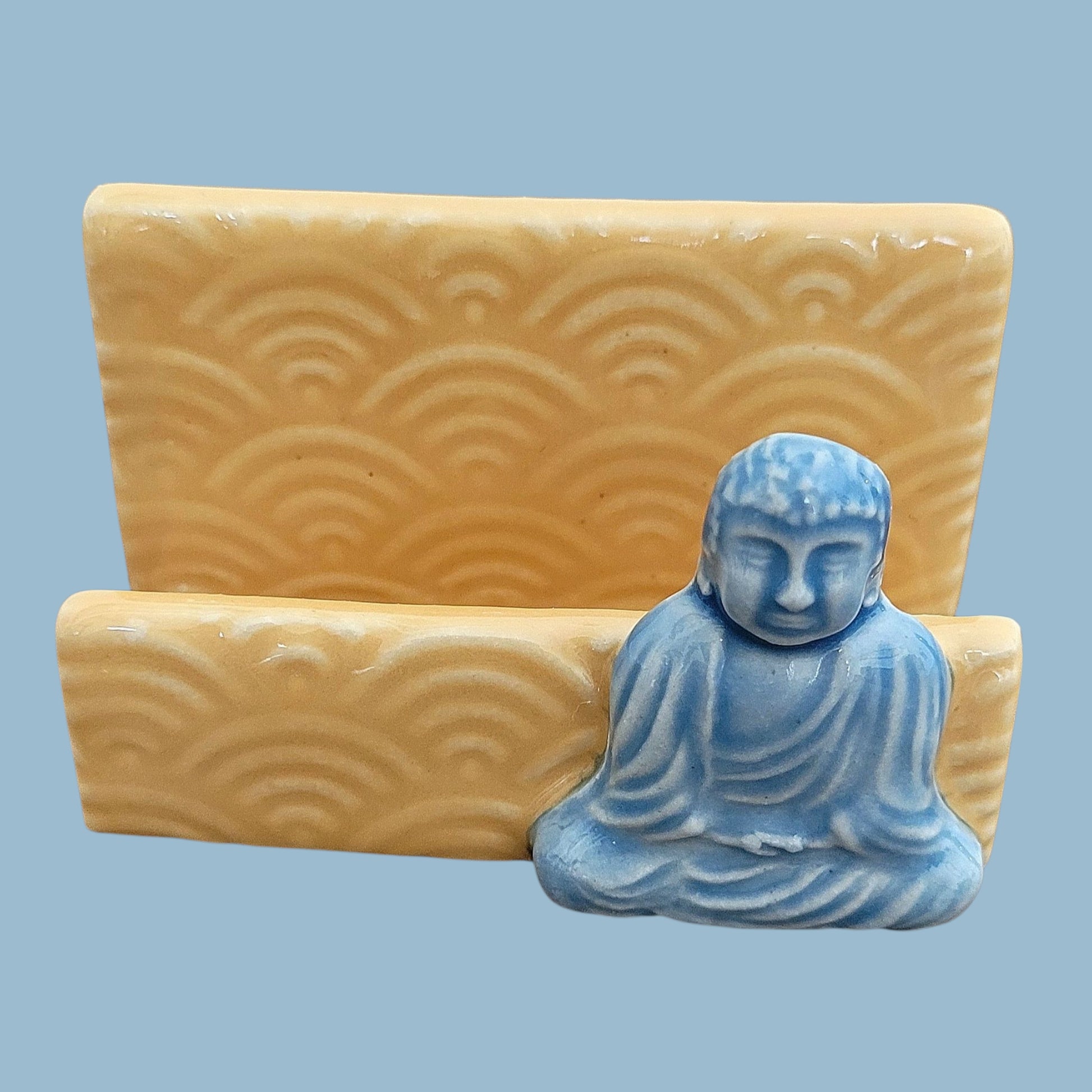 Blue Buddha statue on a yellow stand with wave patterns against a light blue background