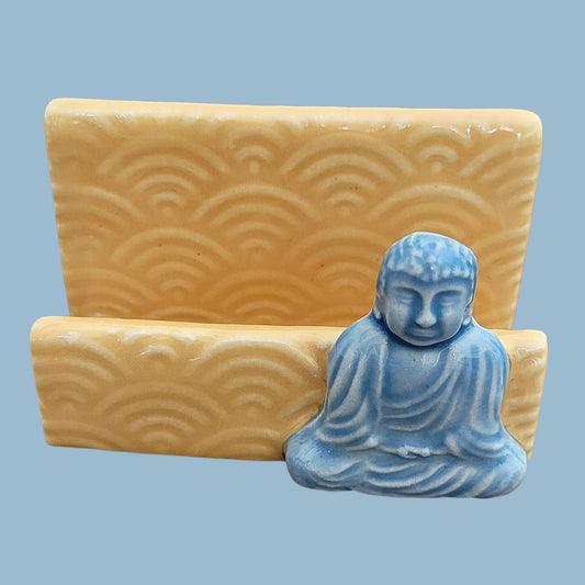 Blue Buddha statue on a yellow stand with wave patterns against a light blue background