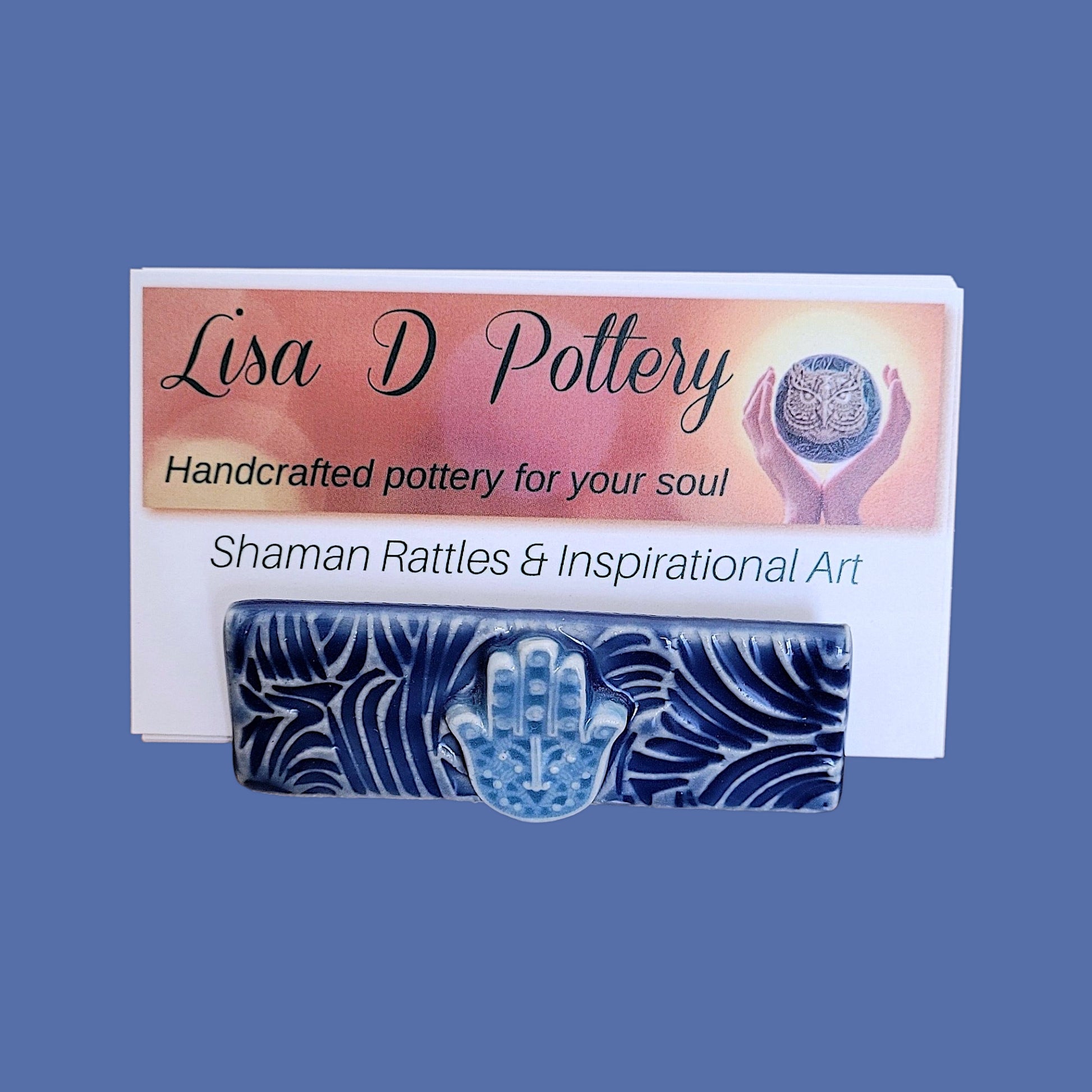 Hamsa hand business card holder in blue and white on a blue background shown holding Lisa D Pottery business cards