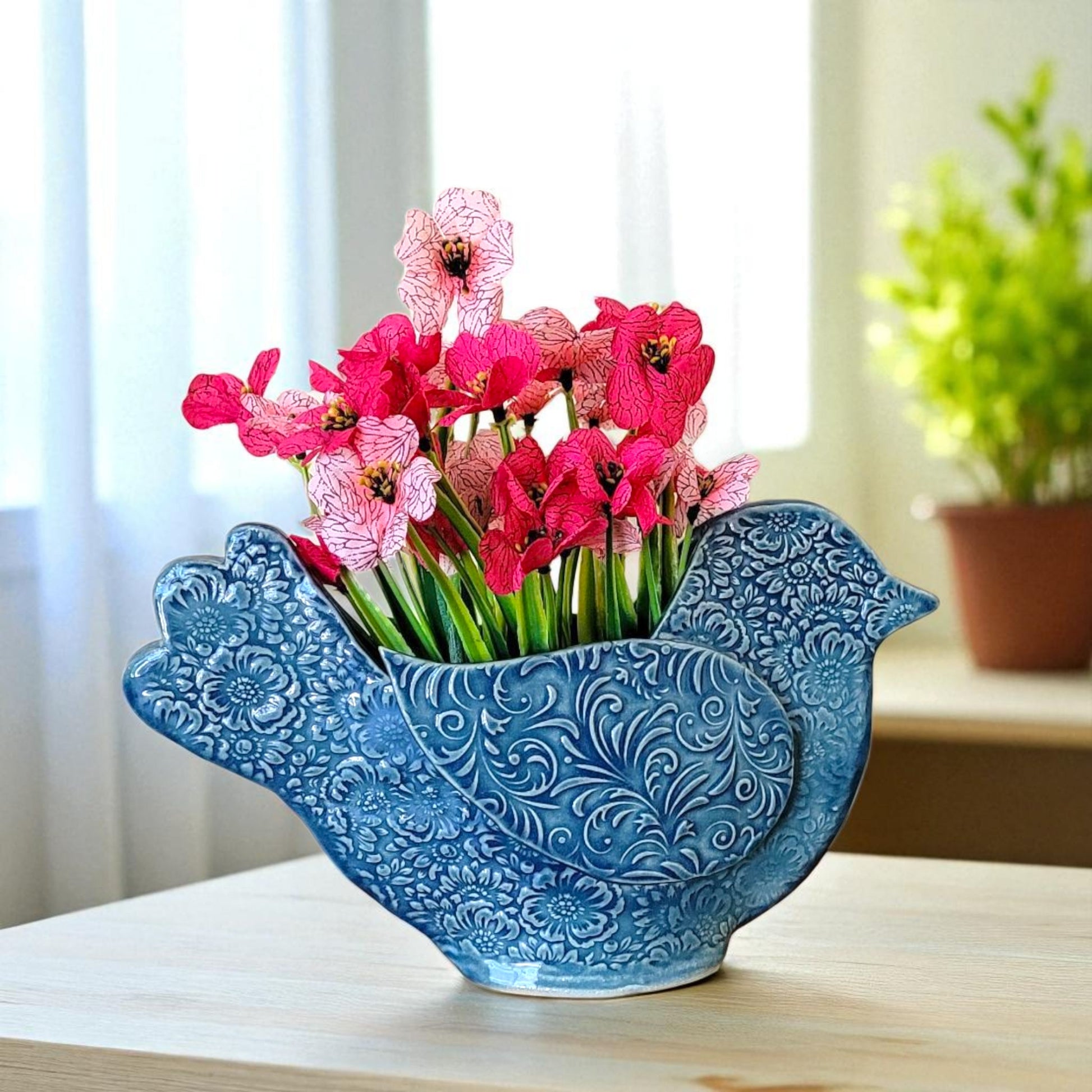 Blue bird-shaped vase with pink flowers on a wooden surface