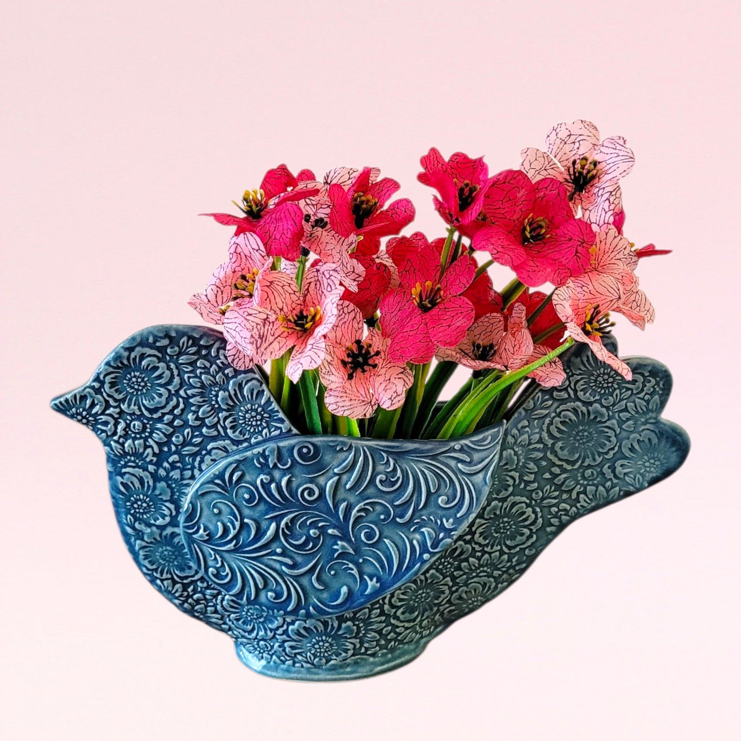 Decorative blue bird-shaped vase with pink flowers on a light pink background