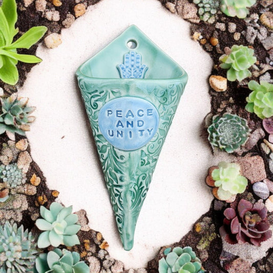 Decorative wall vase with 'Peace and Unity' text surrounded by succulents
