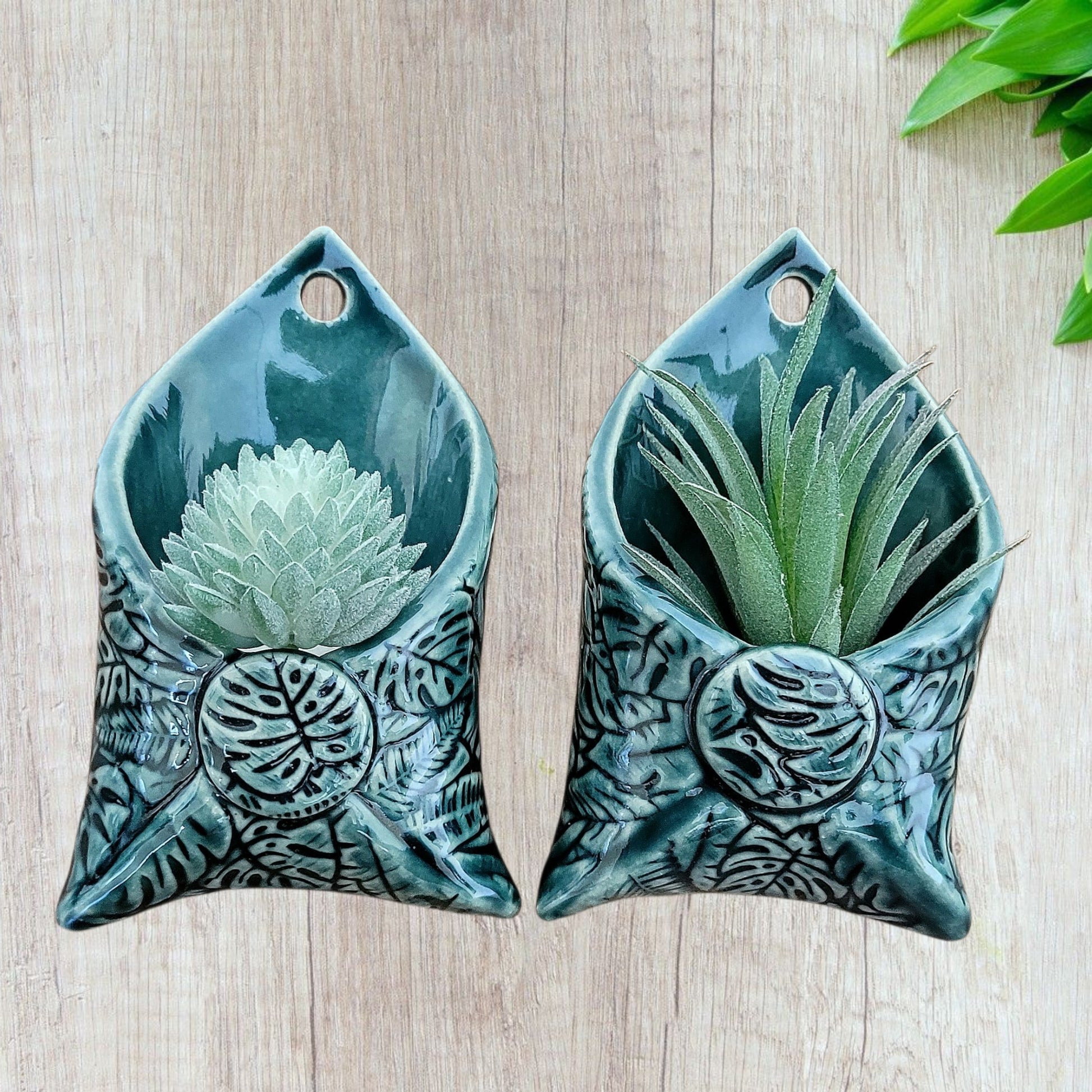 Two dark green ceramic wall planters with succulents on a wooden surface.