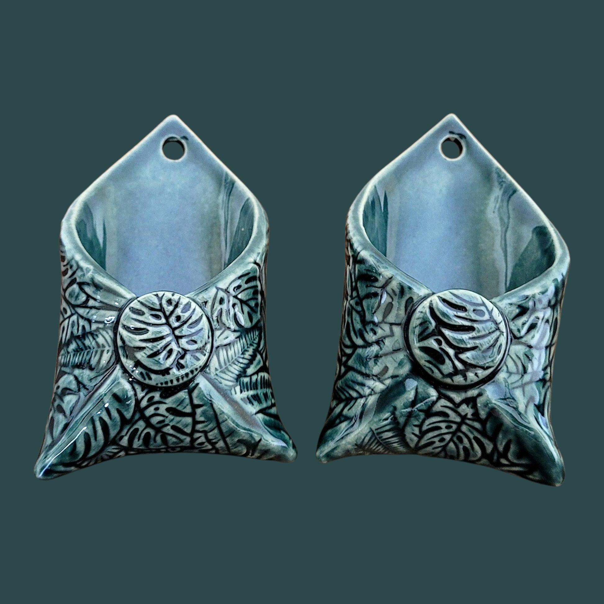 Two ceramic wall hangings with leaf patterns on a dark green background