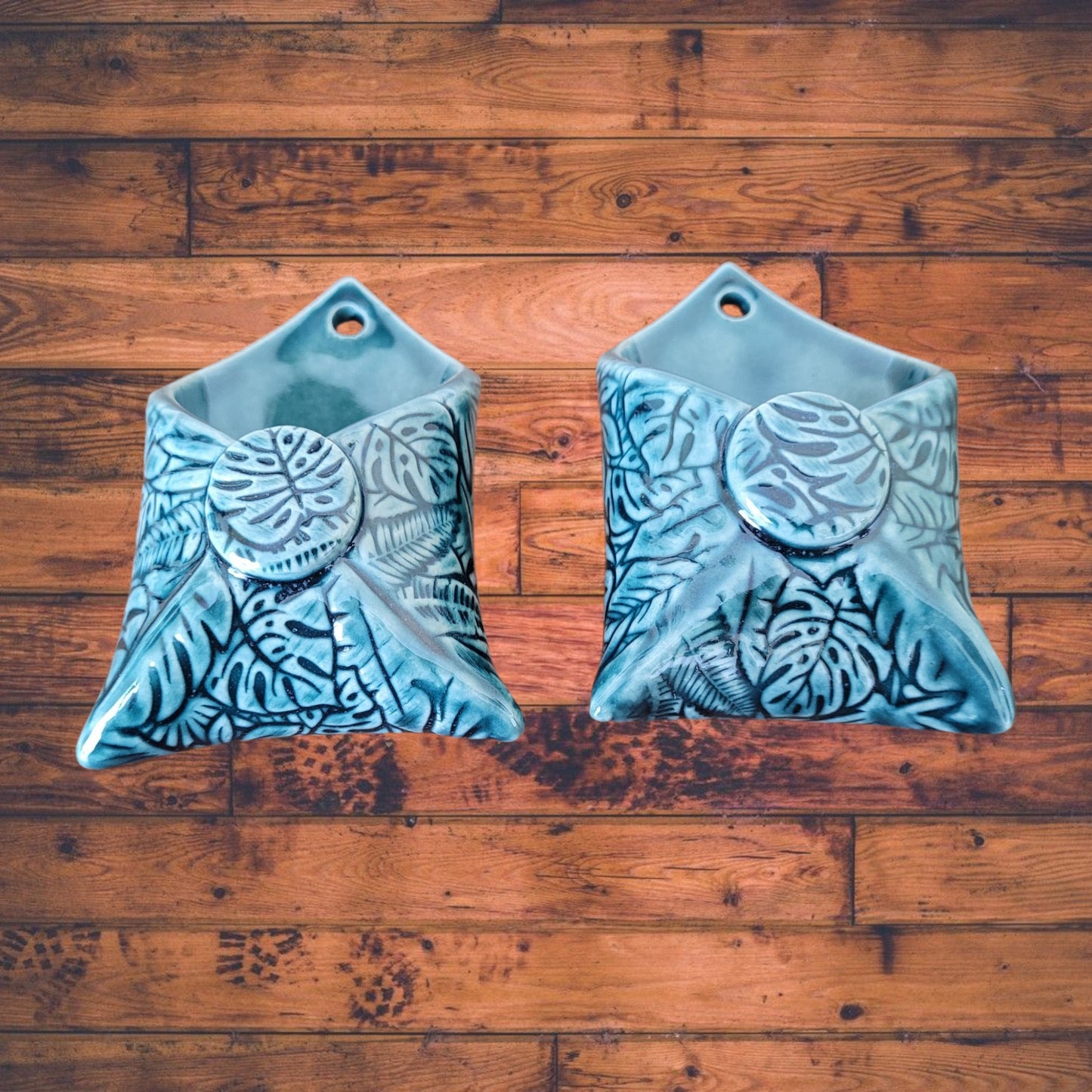 Two dark green ceramic wall hangings with leaf patterns on a wooden surface