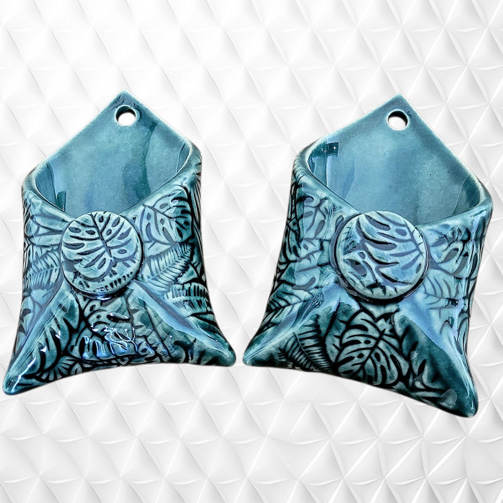 Two dark green ceramic wall hangings with leaf patterns on a white textured background