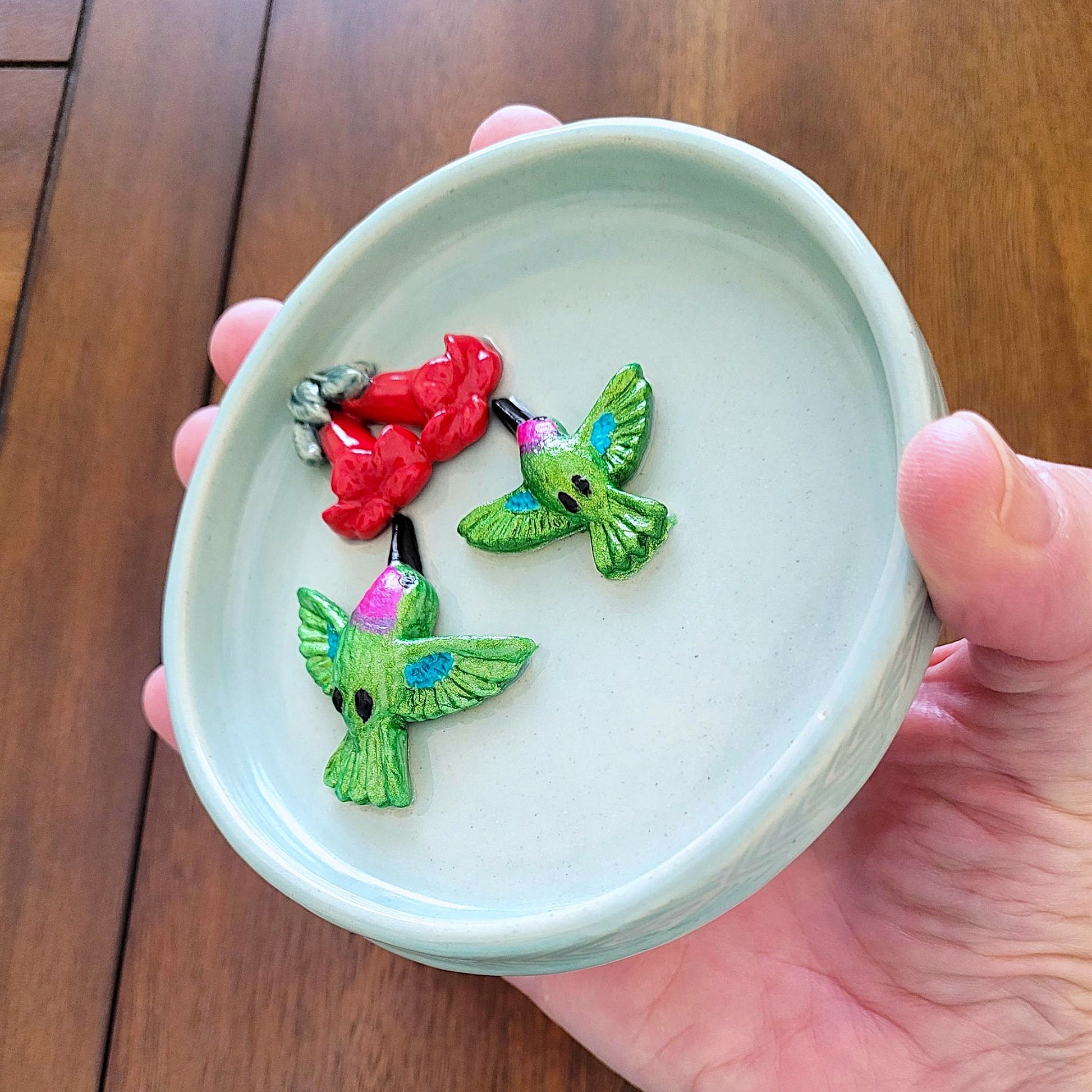 Colorful hummingbirds on a small round blue ceramic dish held by a hand against a wooden background