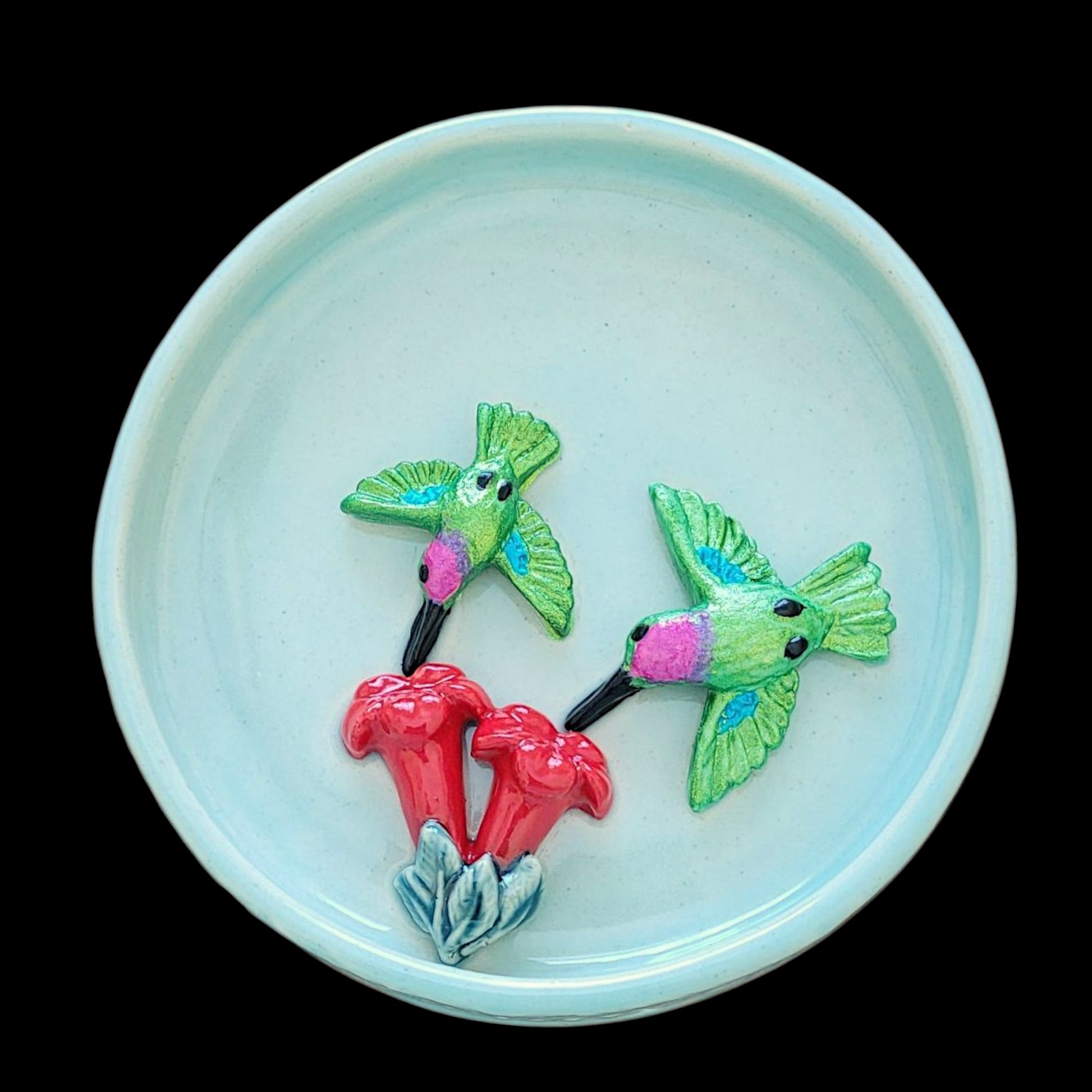 Decorative blue ceramic dish with green hummingbirds and red flowers on a black background