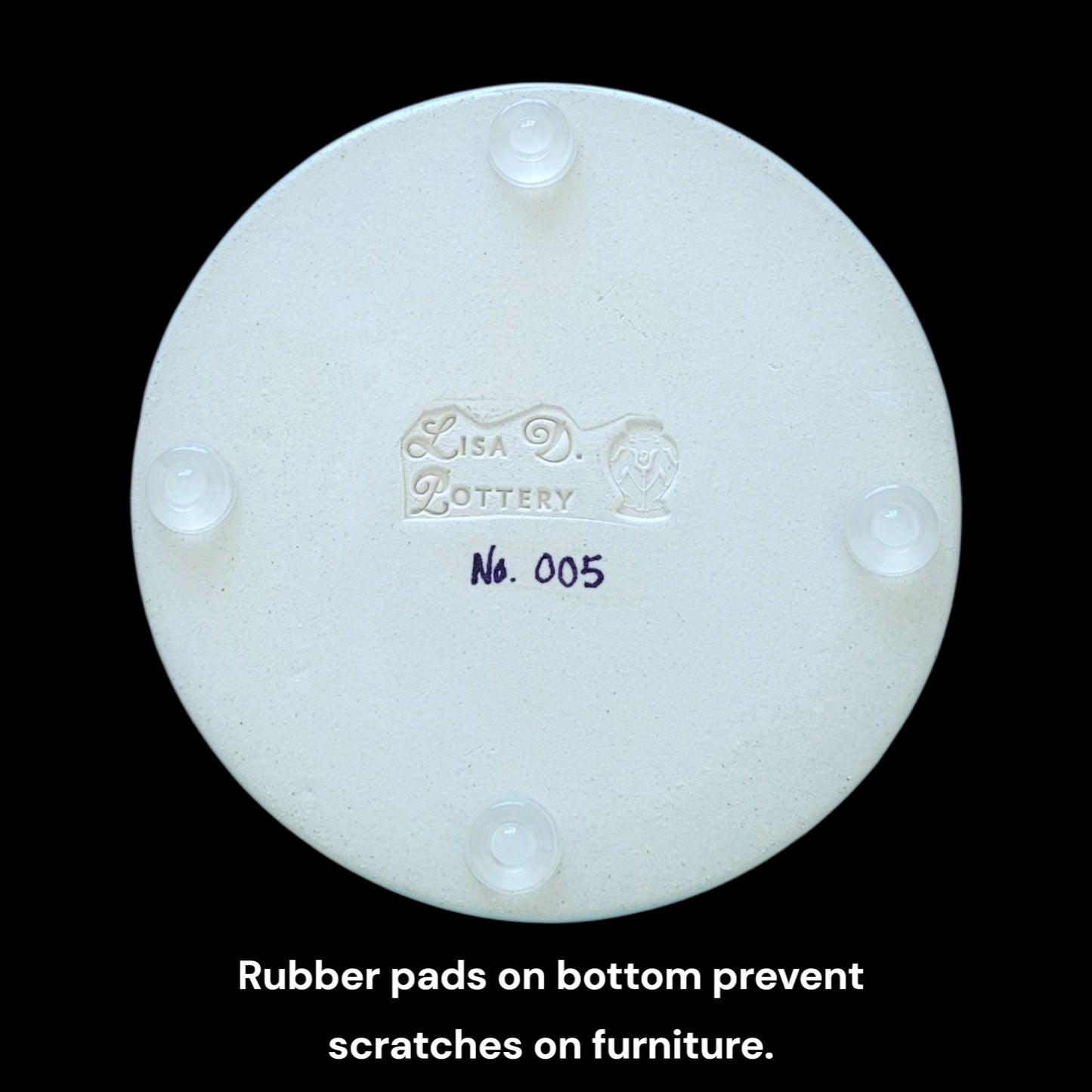 Bottom of trinket dish with round clear rubber pads showing 'Lisa D Pottery' branding and product number on a black background.