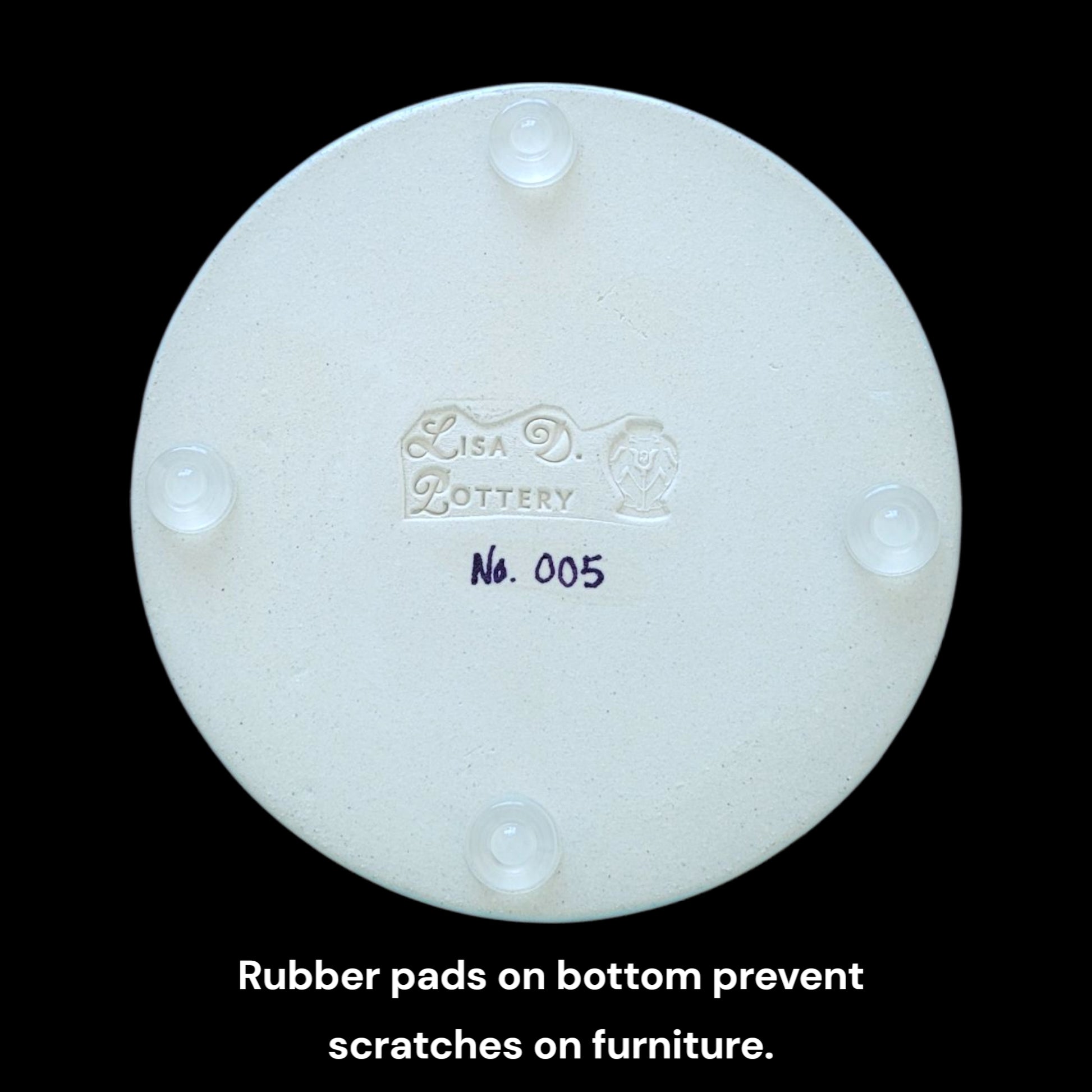 Bottom of trinket dish with round clear rubber pads showing 'Lisa D Pottery' branding and product number on a black background.