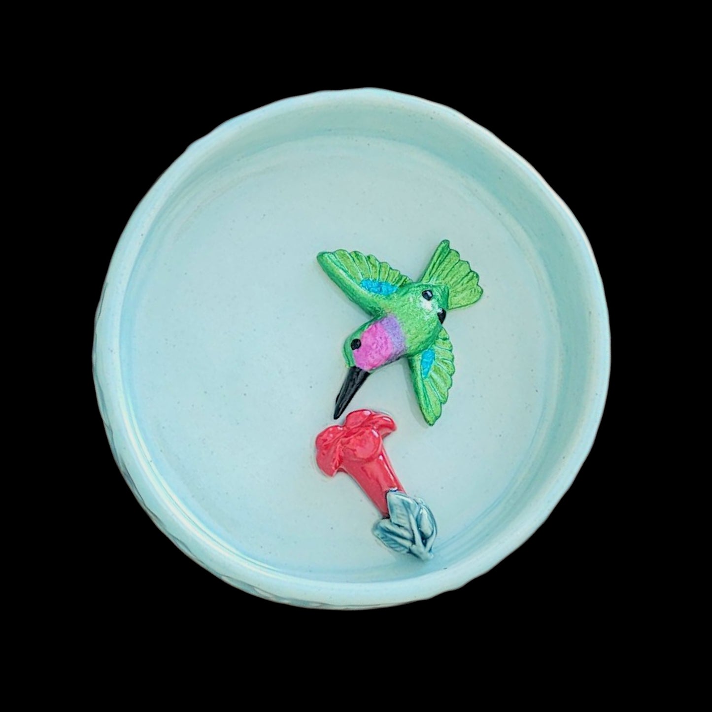 Decorative blue ceramic dish with a green hummingbird and red trumpet flower on a black background