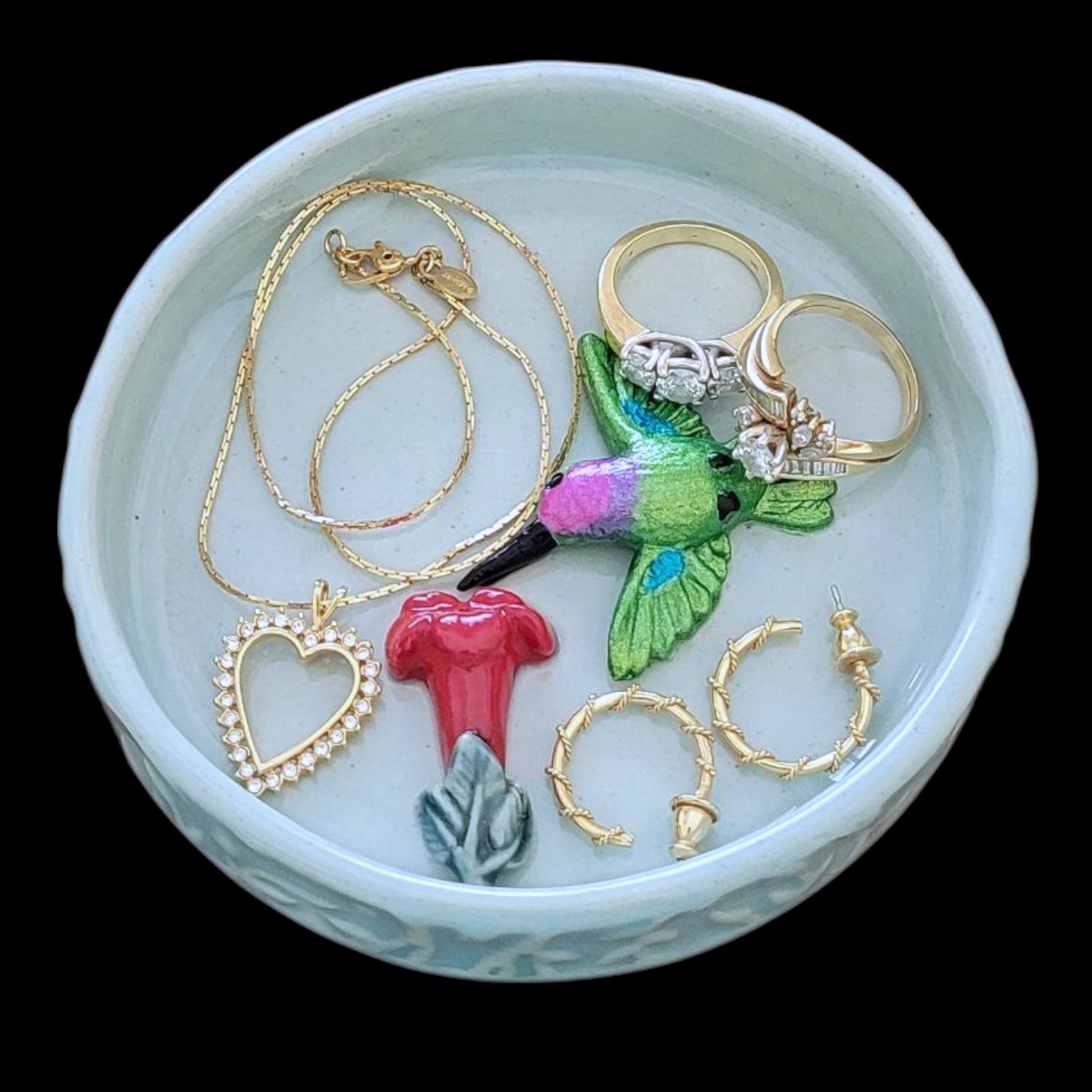 Jewelry set including necklaces, rings, and earrings sitting in a light blue ceramic dish on a black background.